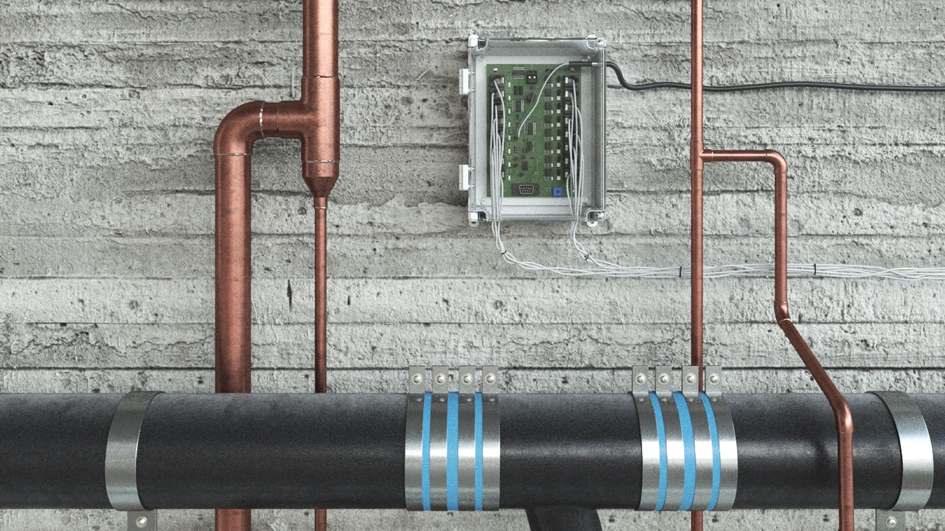 Close-up of copper and black water pipes mounted on a concrete wall, with a small control box connected to the system.
