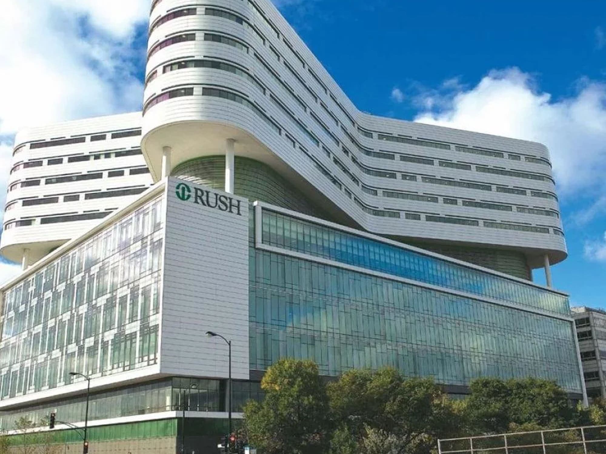 Modern hospital building with a distinctive curved architectural design, featuring glass façades and multiple stories under a bright blue sky.