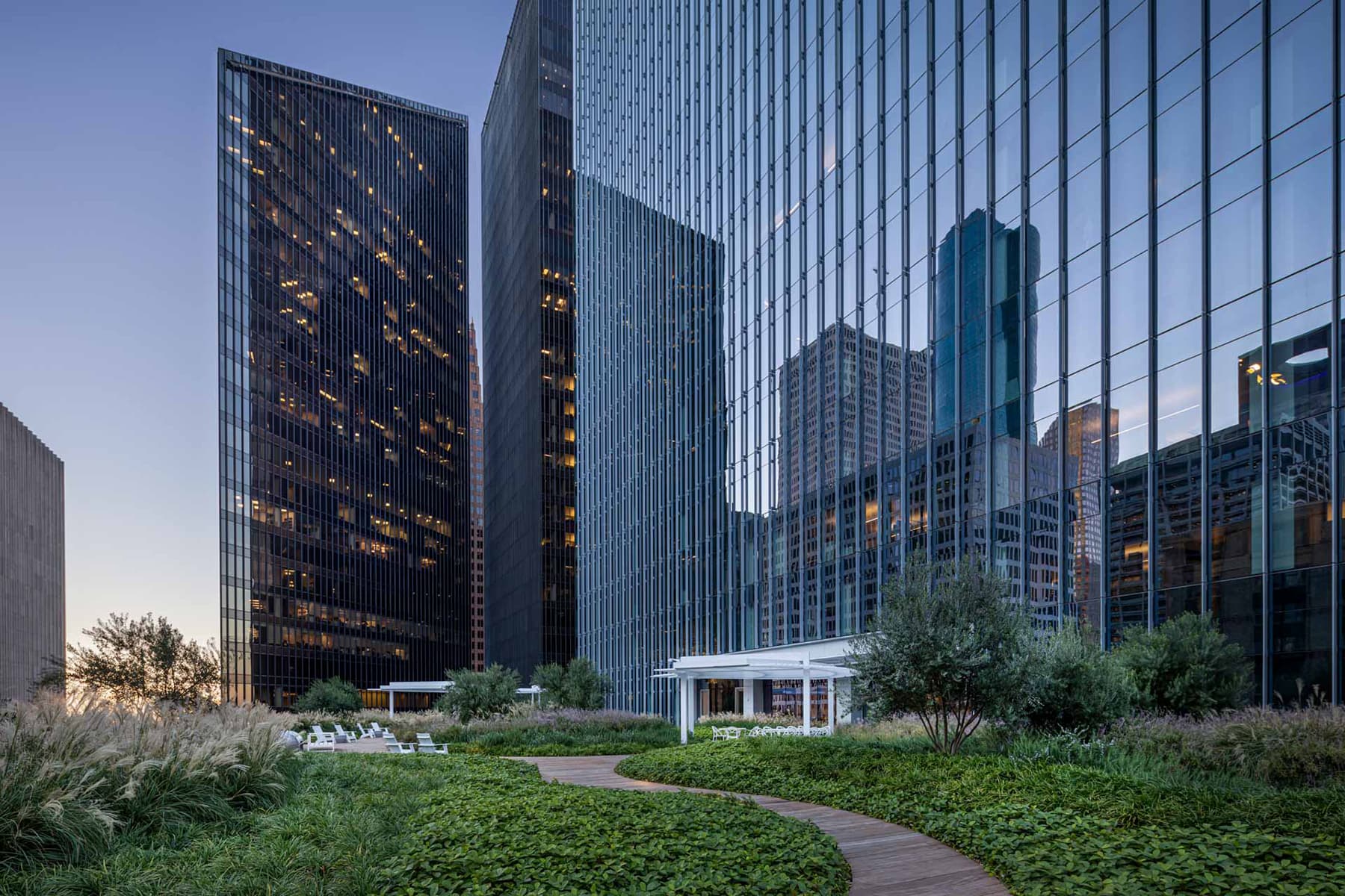 Street view of the glass exteriors of the Capital Tower with greenery and a wooden bridge