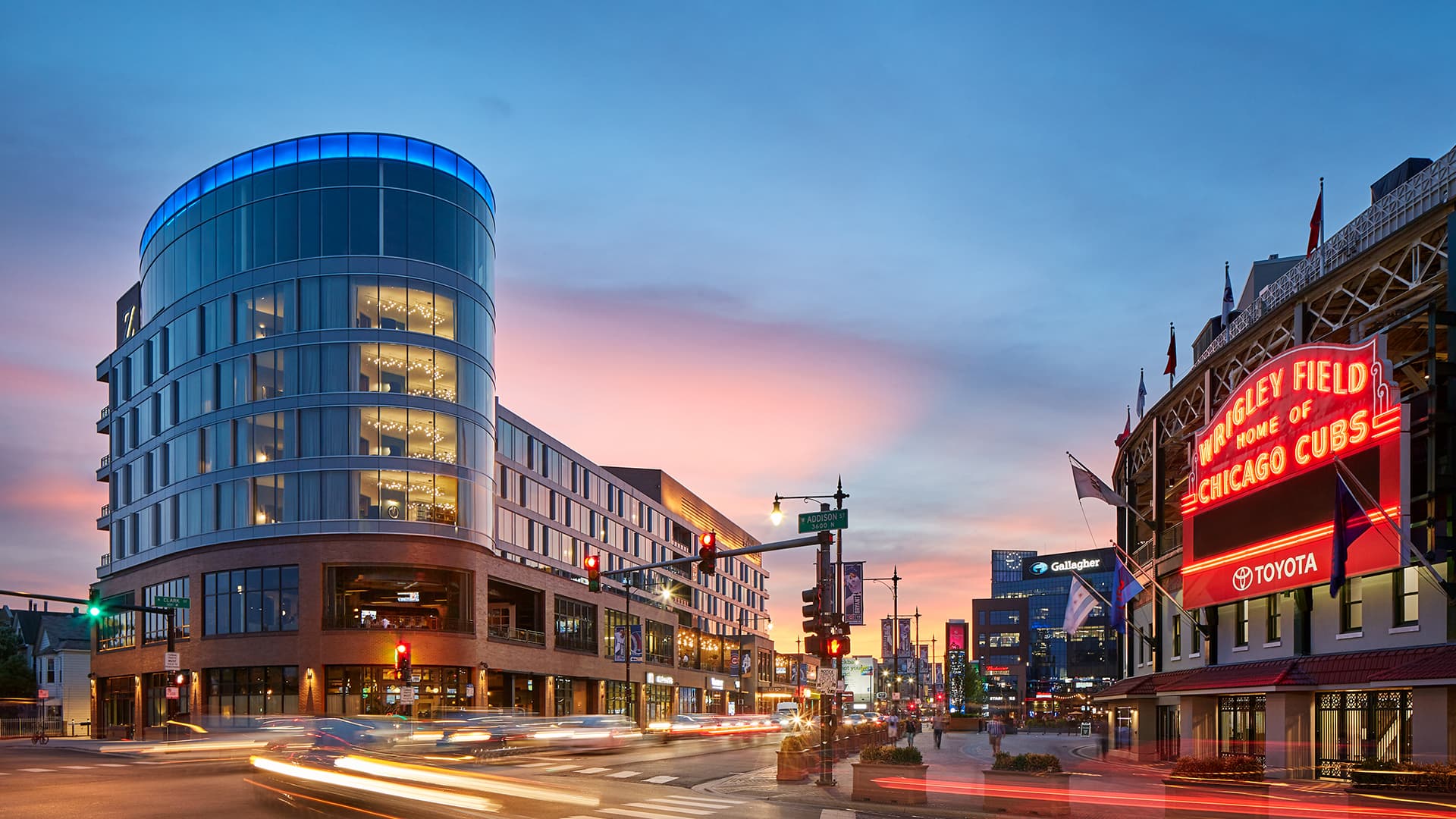 Street view of a busy street featuring the Hotel Zachary brick and glass exterior an the left and Wrigleyfield entrance on the right