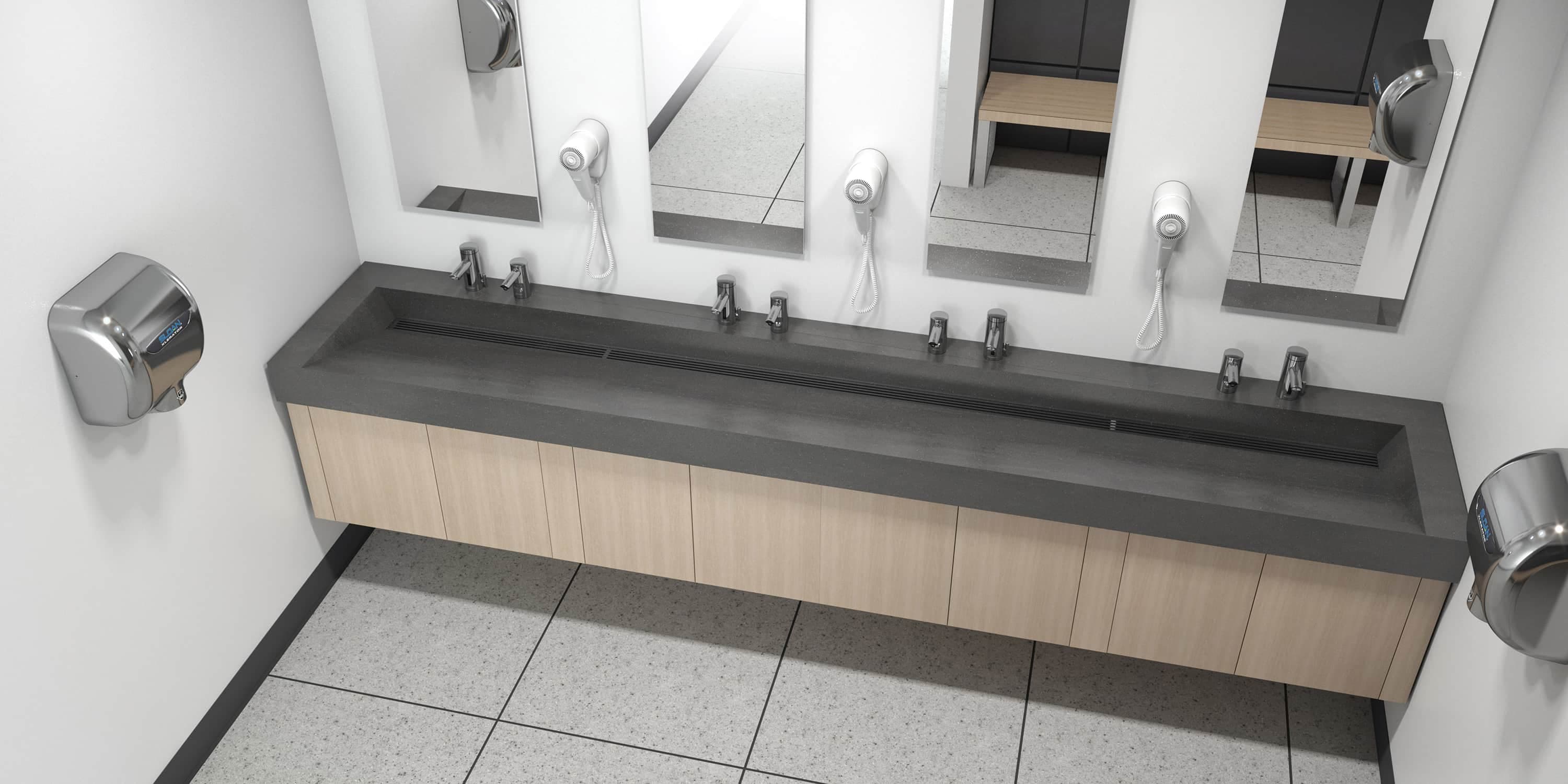 Modern restroom featuring a long solid-surface sink countertop with four touch-free chrome faucets and matching soap dispensers beneath wall-mounted mirrors. Light wood cabinetry below provides storage, and stainless steel hand dryers are mounted on both side walls.