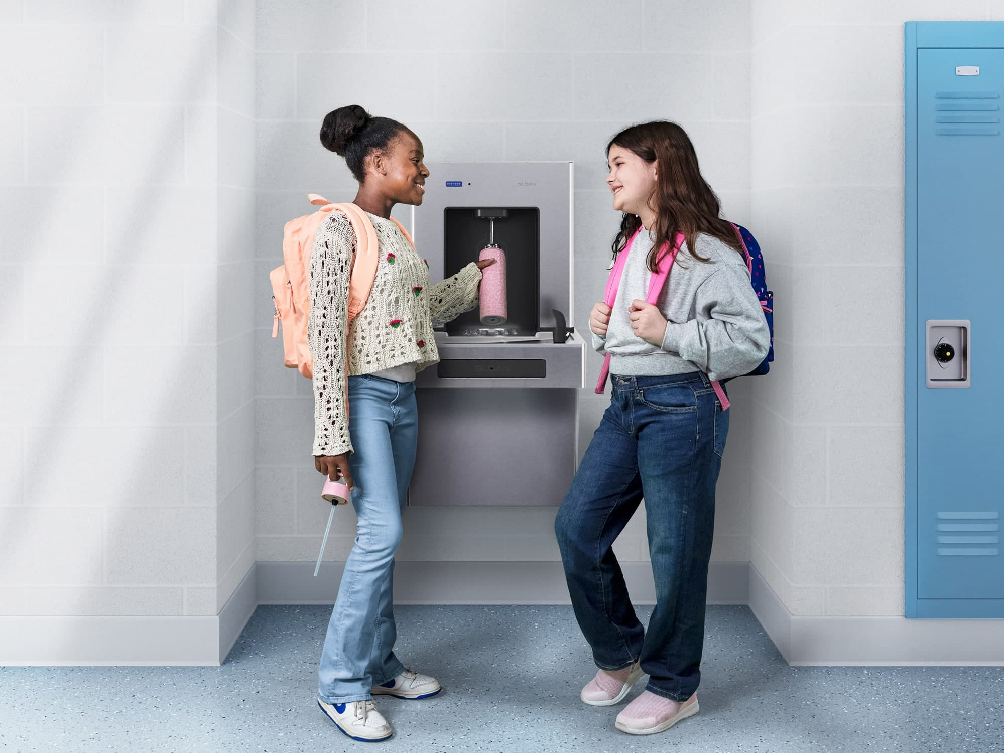 Two elementary school girls chatting and filling up their water bottle from a DropSpot