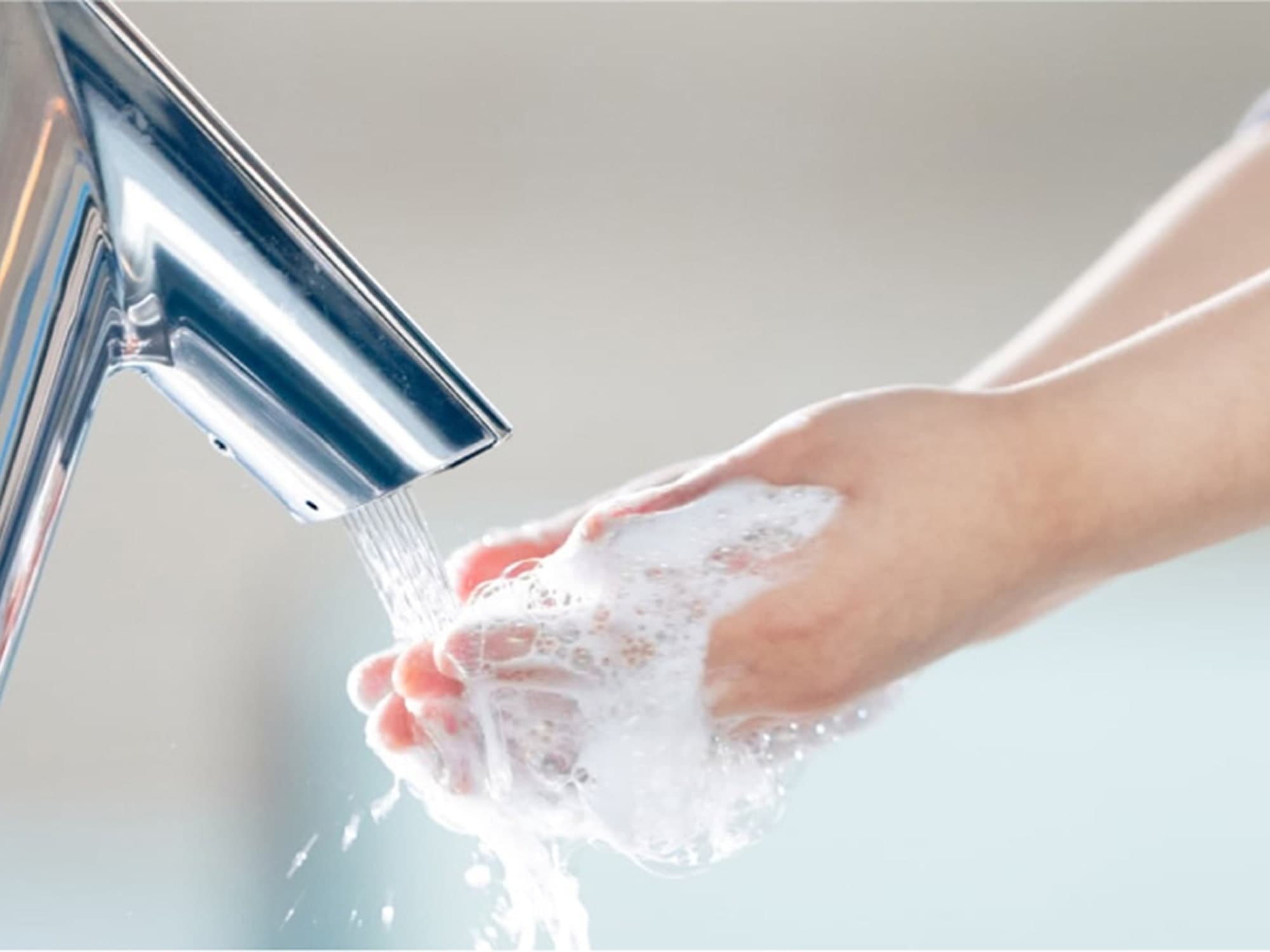 close up of person washing hands with water and soap using a Sloan BASYS faucet